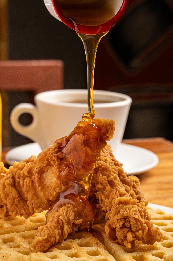 Honey being poured over fried chicken and waffles